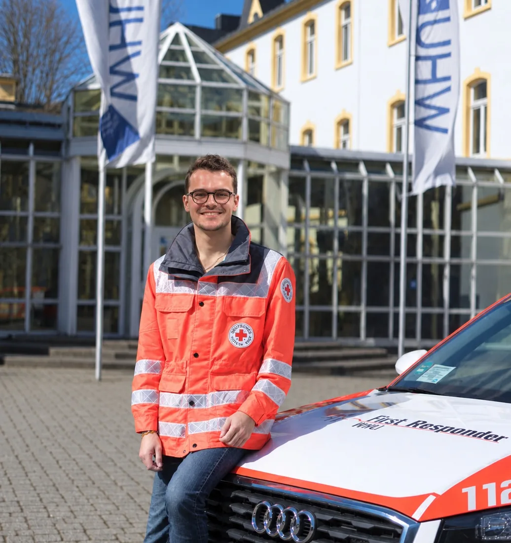 Fabian Tingelhoff in a German Red Cross jacket, sitting on a first responder vehicle in front of WHU